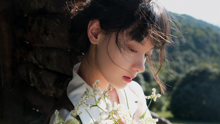 一位身着绿色连帽衫和白色短裙的黑色长发美女一手拿着鲜花一手拿着老式胶片相机她侧身面对观众站在郁郁葱葱的草地上在绿色背景的衬托下脸上洋溢着幸福的微笑_美女照片背影侧面